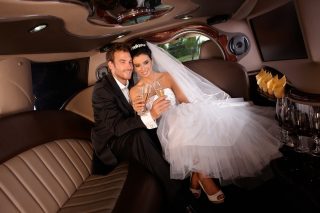 Romantic young couple sitting in limo on wedding-day, clinking glasses.